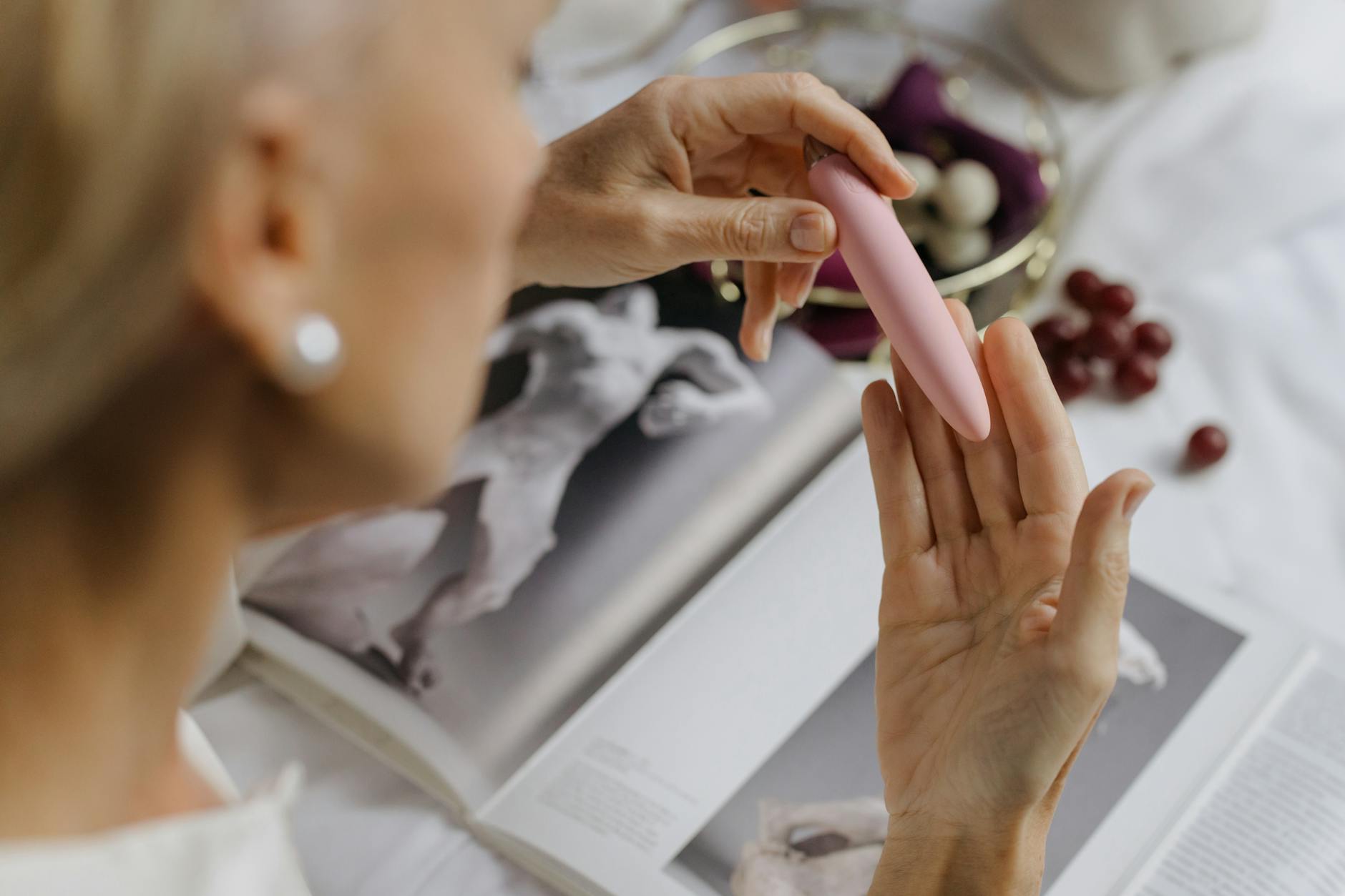 Woman holding a pink vibrator with art books in background, representing intimate pleasure without penetration