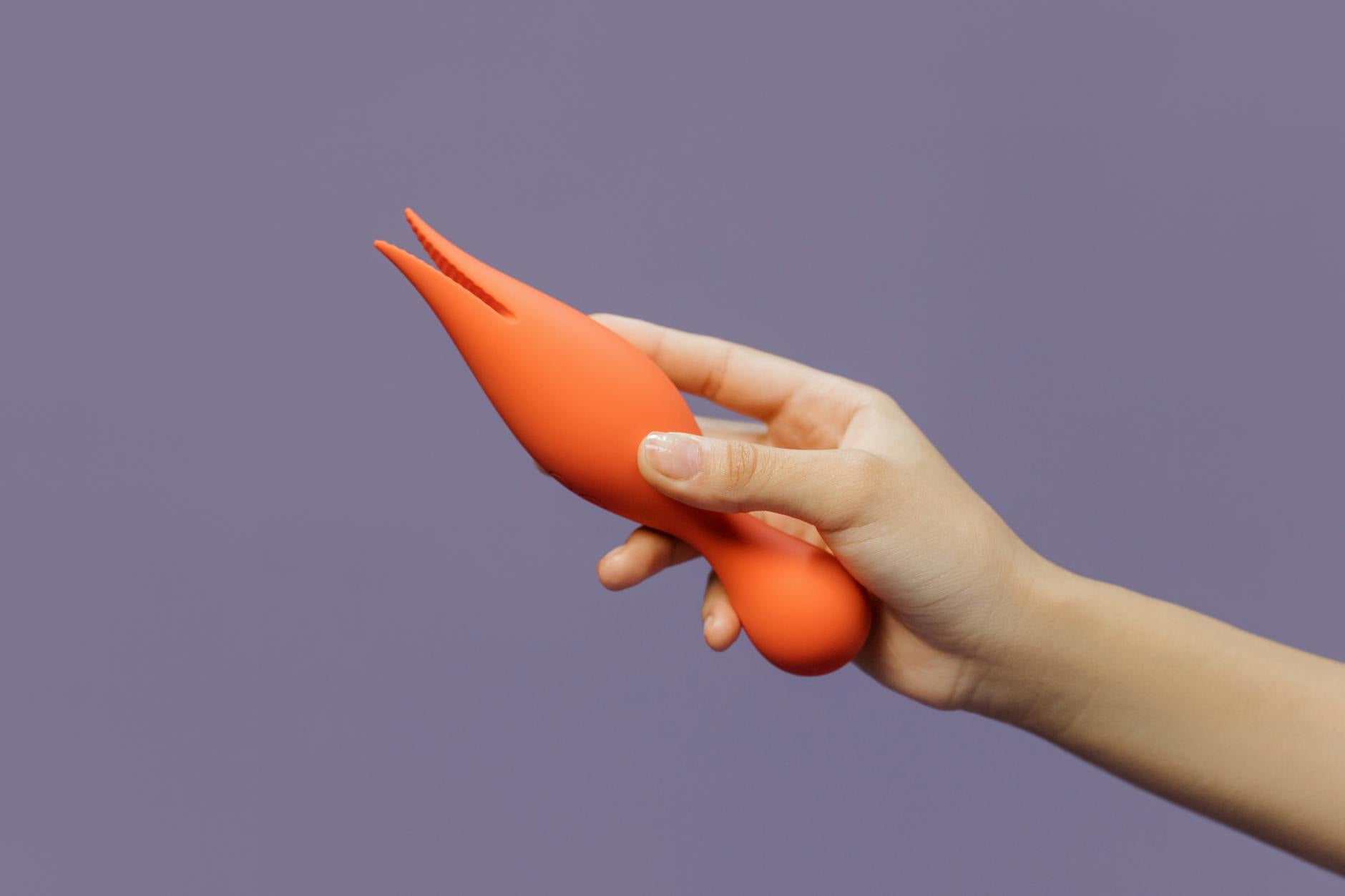 Close-up of a hand holding a lemon vibrator against a minimalistic purple backdrop, showcasing sensual modern design.