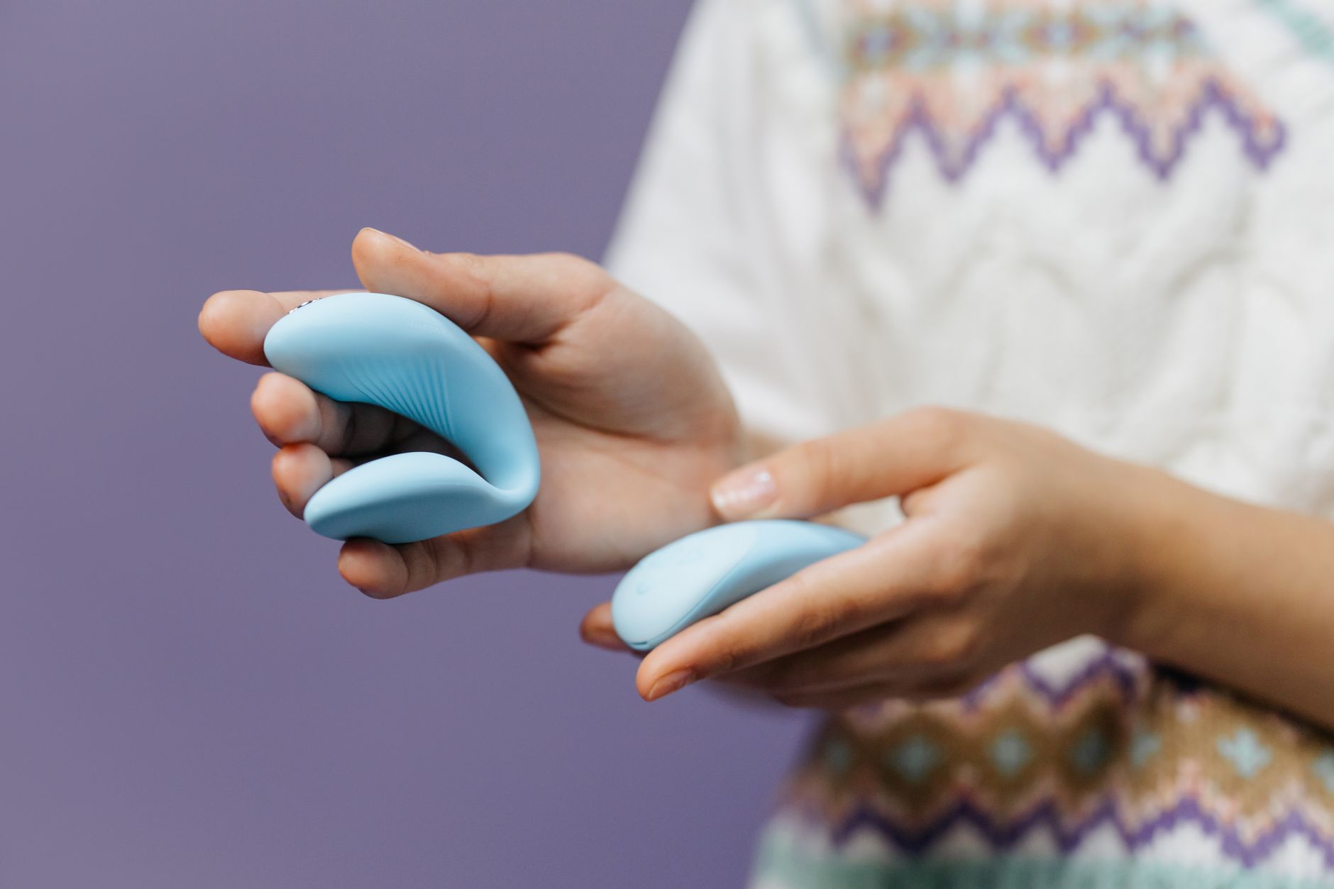 Hand holding a sleek blue clitoral vibrator against a purple background