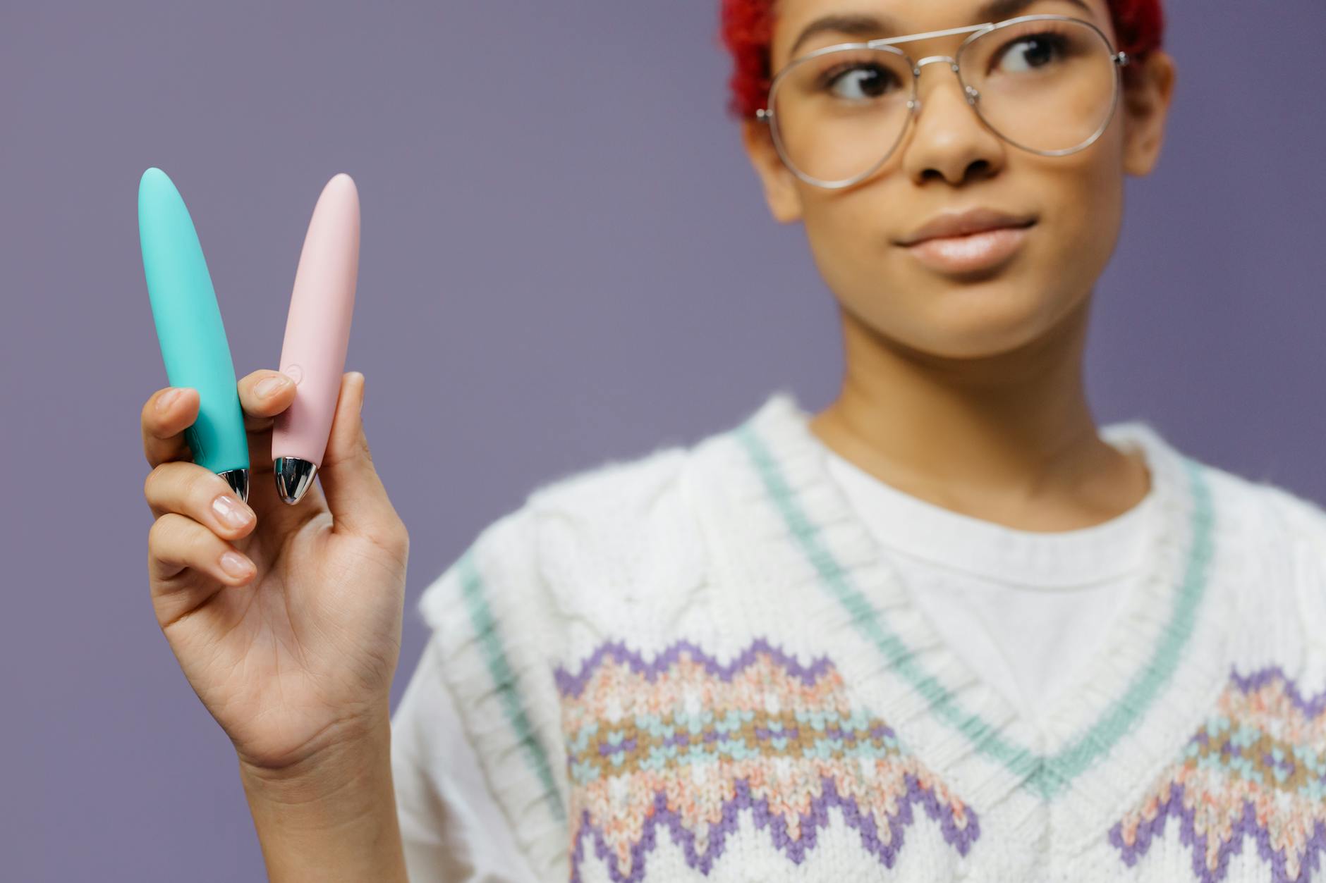 Woman holding blue and pink silicone vibrators thoughtfully