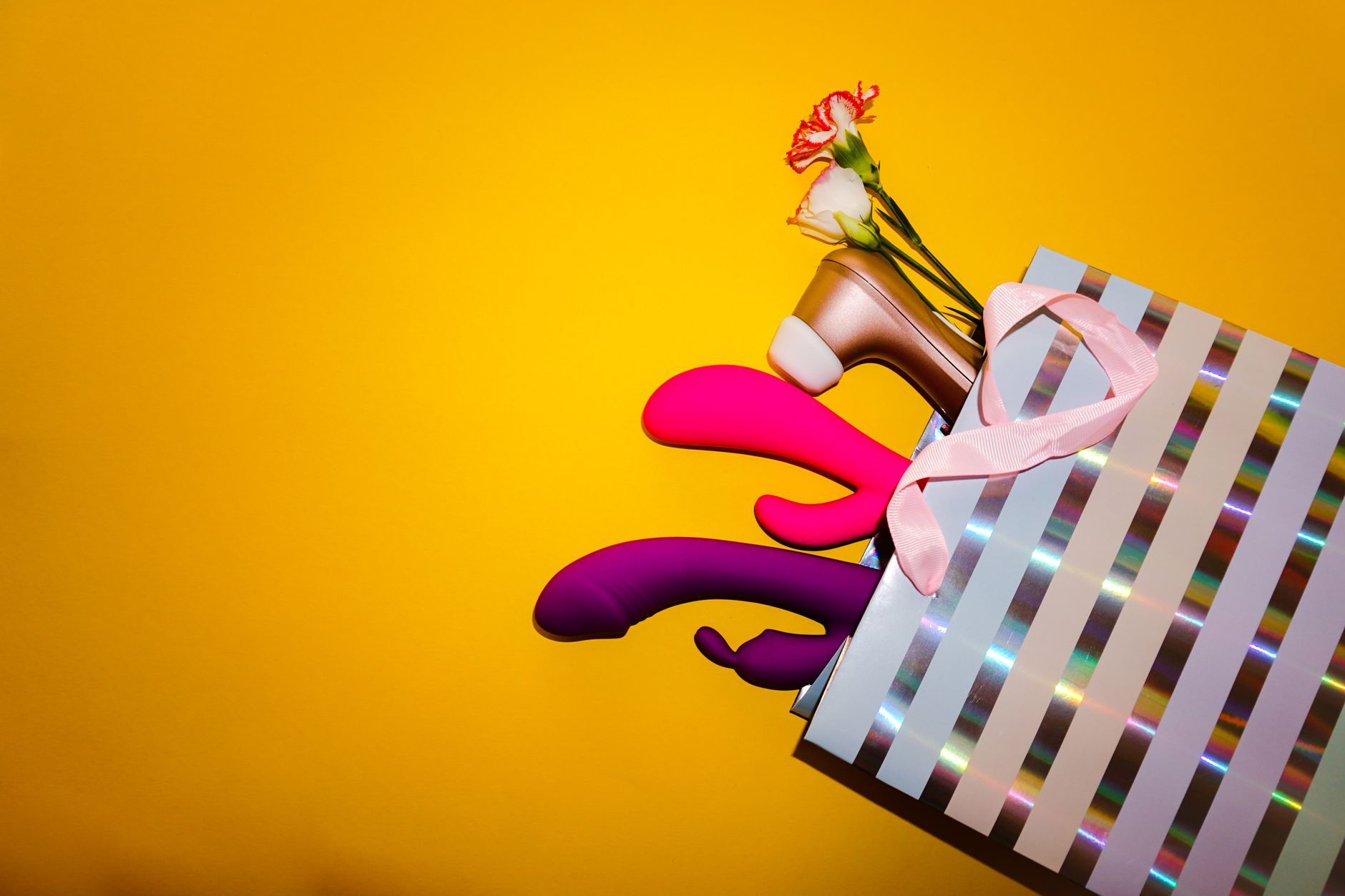 A vibrant collection of colorful sex toys arranged on a bright yellow surface.