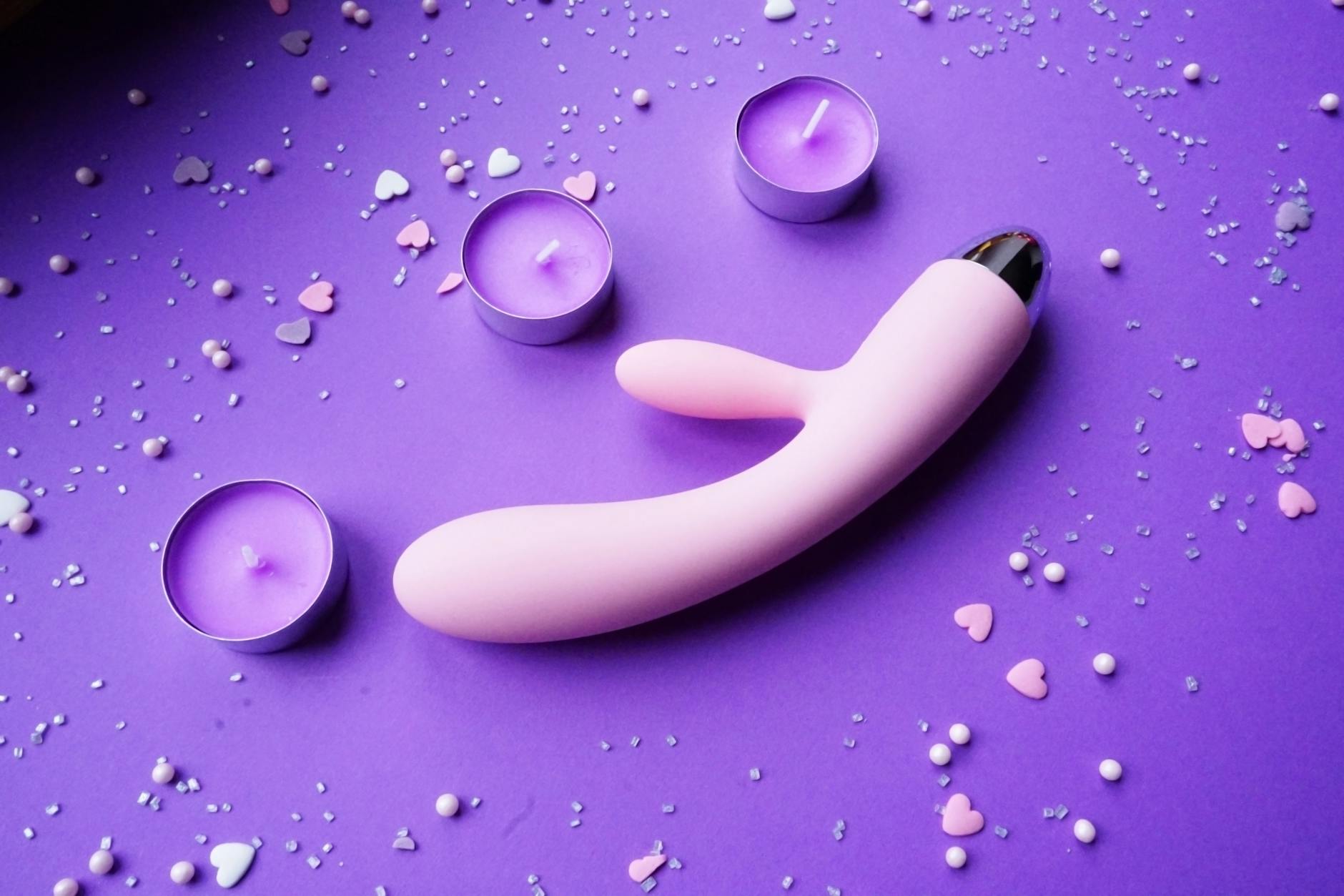 A hand holding a blue silicone toy against a purple background, illustrating intimate self-care and pleasure.